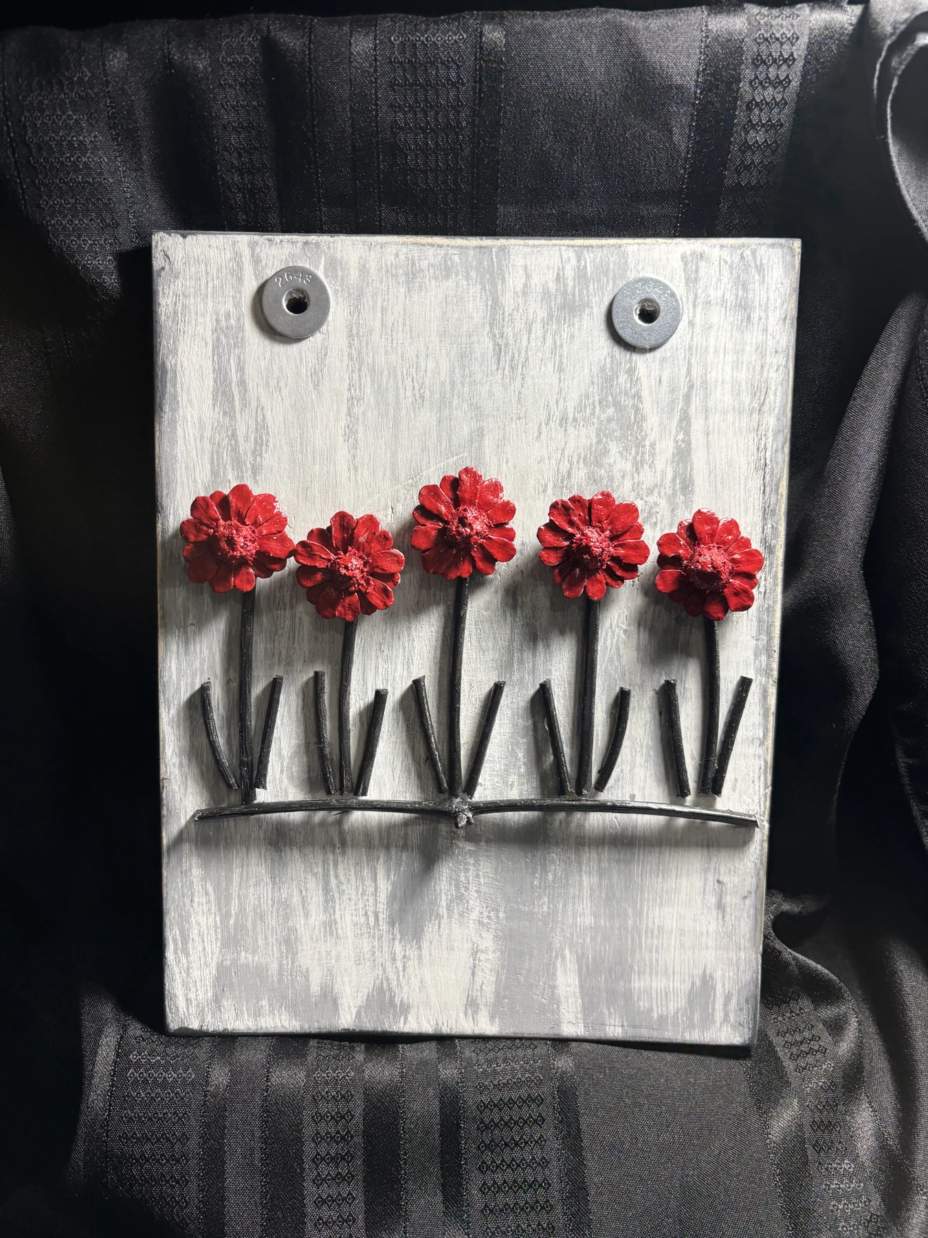 Five red flowers with dark stems on a weathered pale wooden wall piece